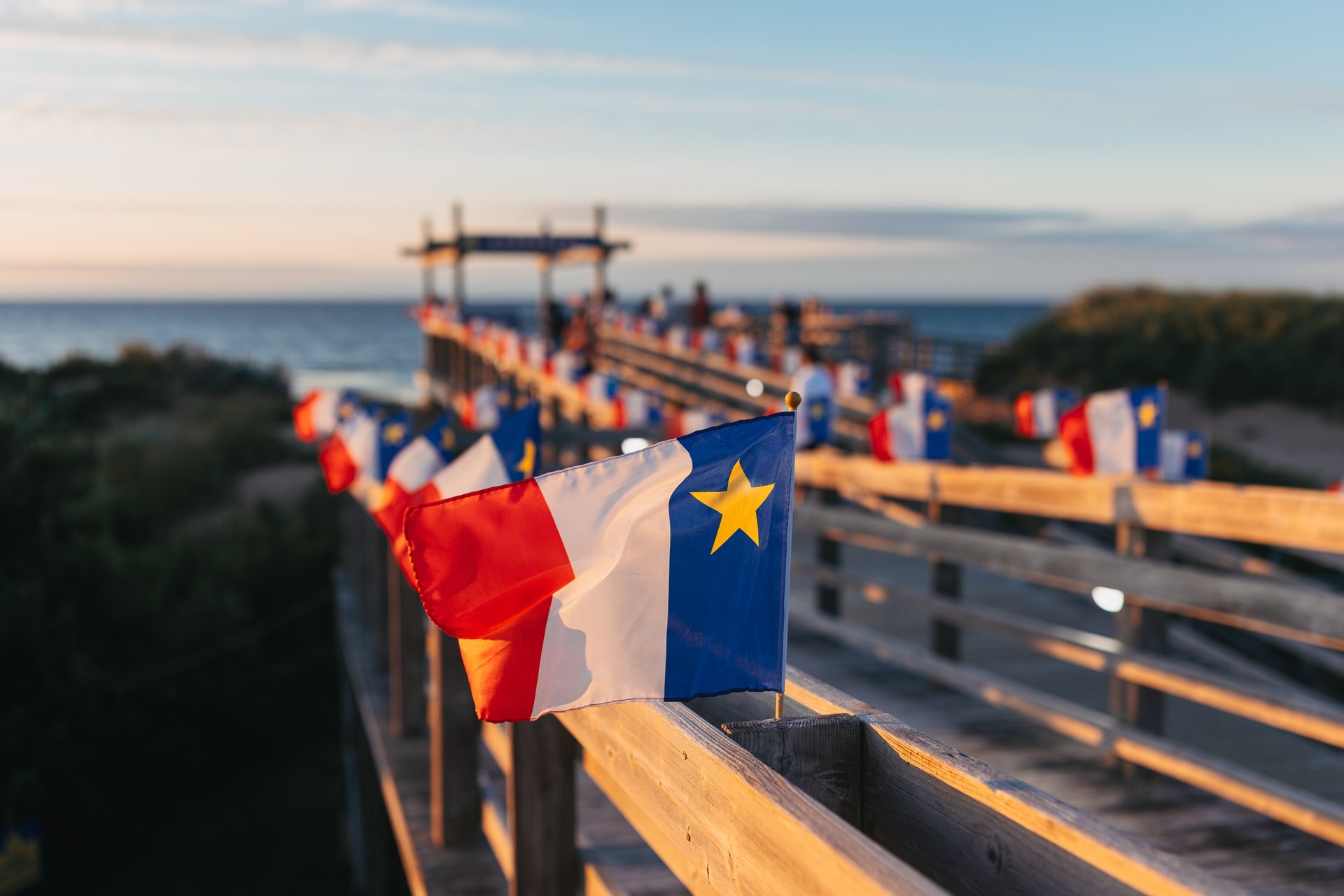 A bridge over sand going towards a beach decorated with Acadian flags
