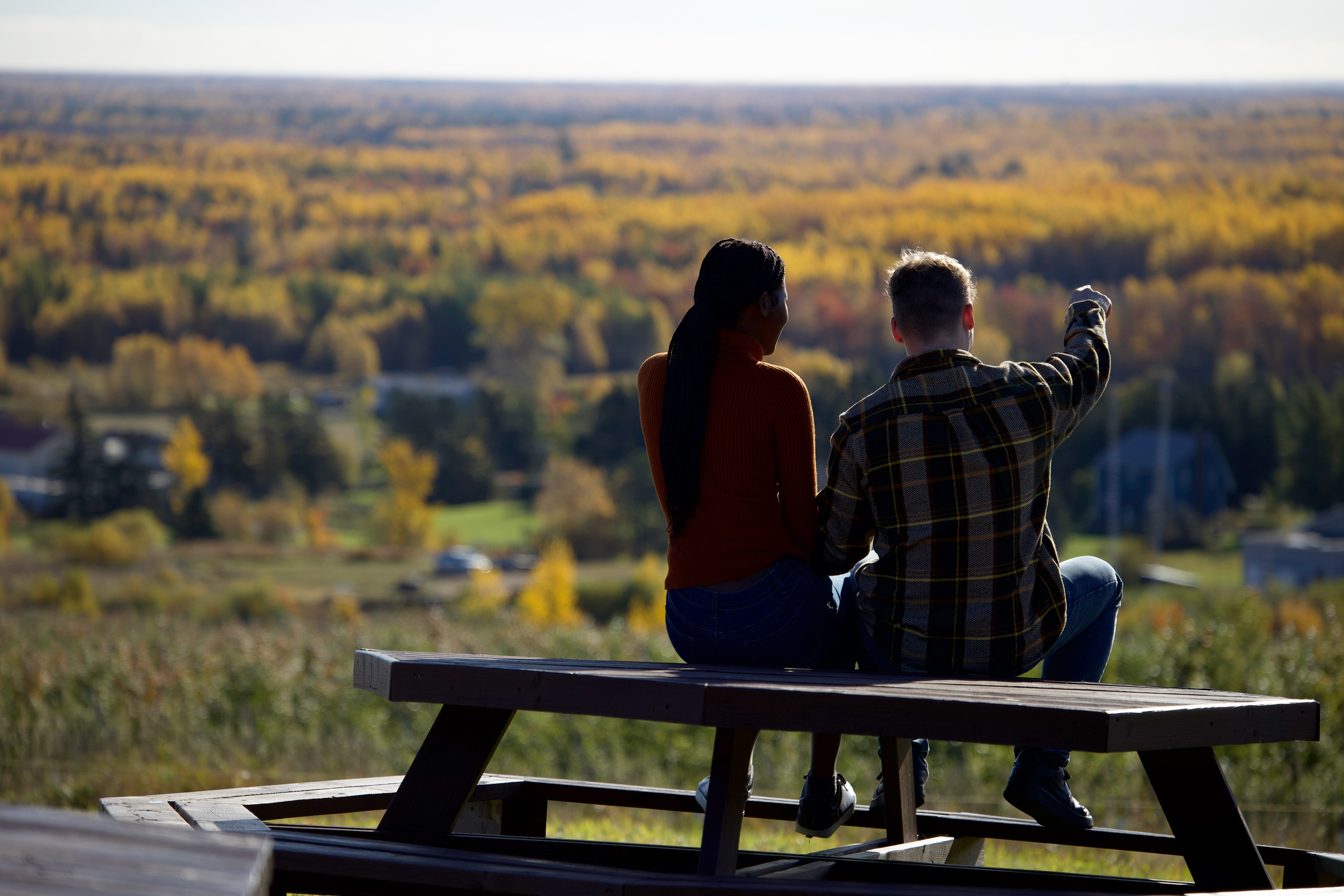 Couple looking over a wooded area from a picnic table on a hill